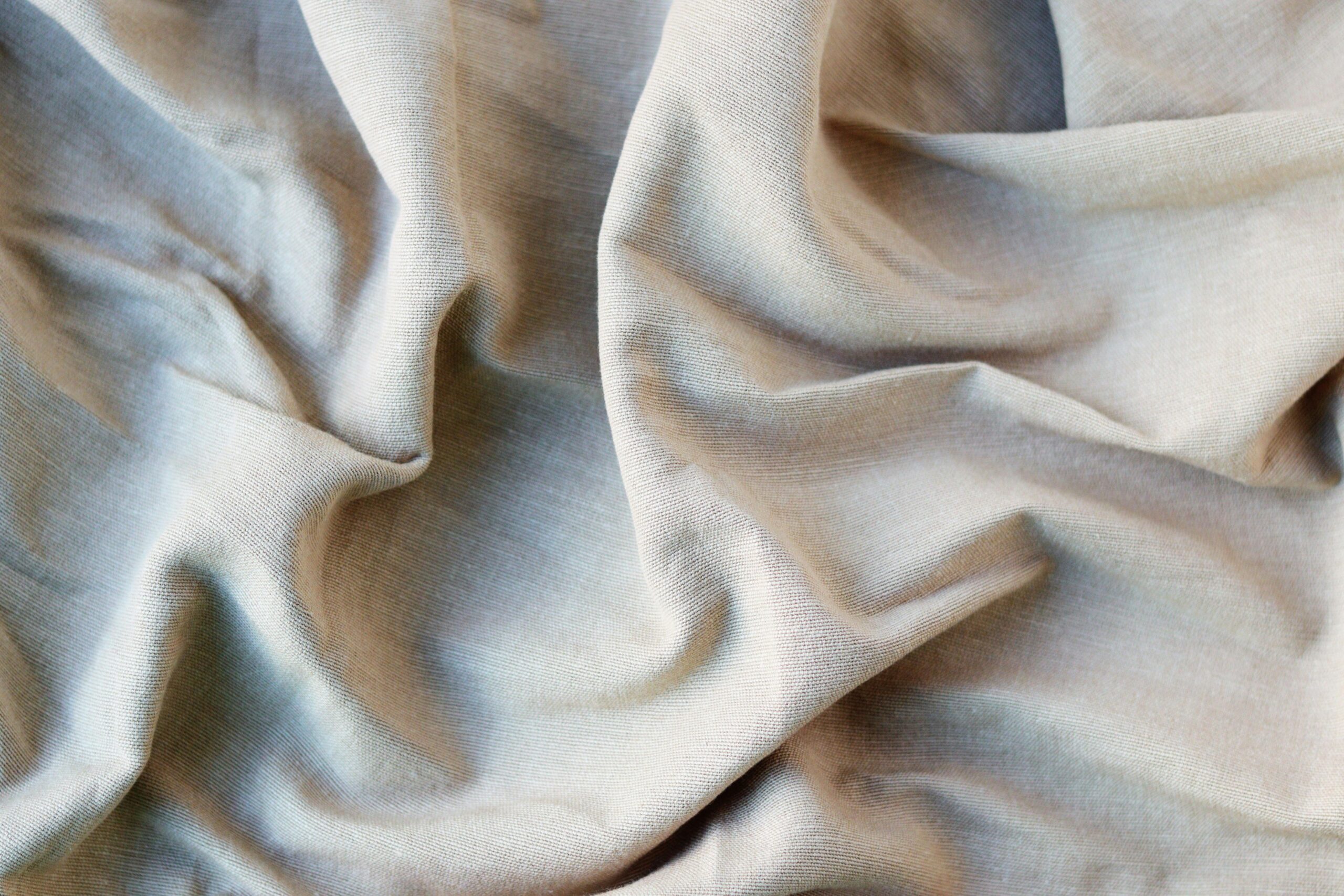 Detailed close-up of light brown crumpled cotton fabric, showcasing its texture and folds.